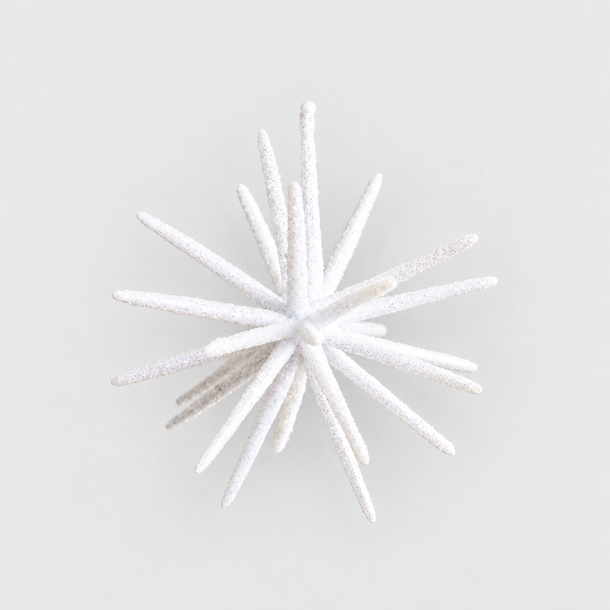 Small white glitter starburst ornament on a plain light grey background