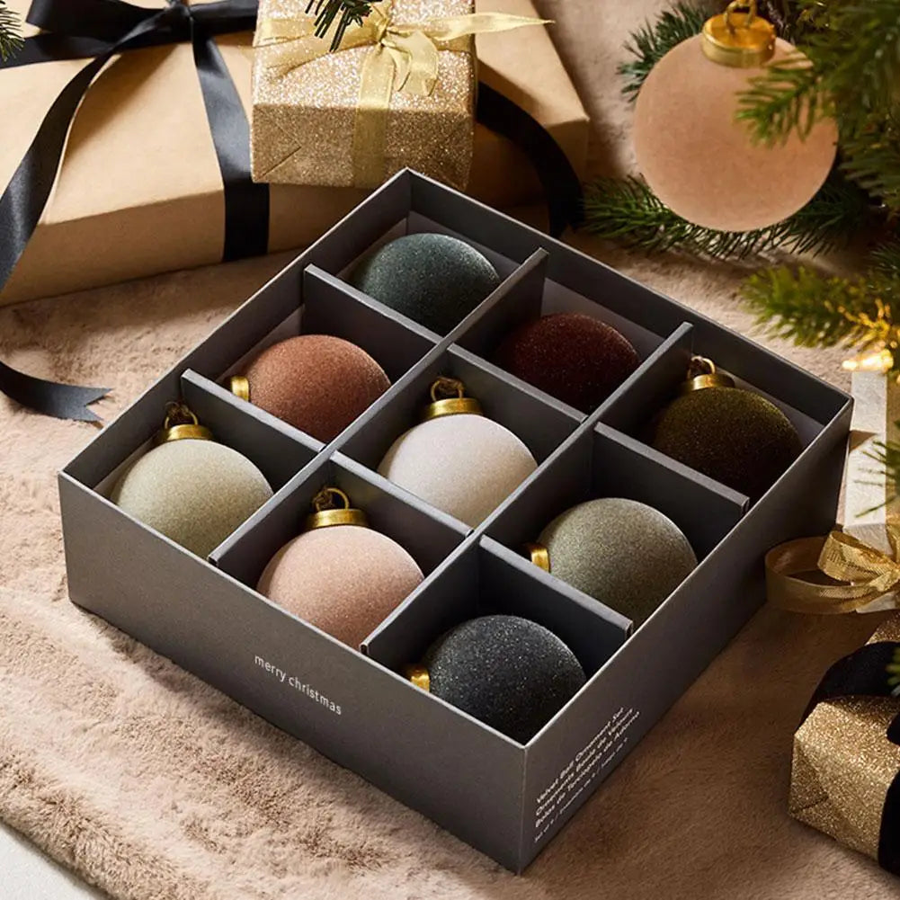 Open gift box of nine velvet baubles on a soft rug beside wrapped presents