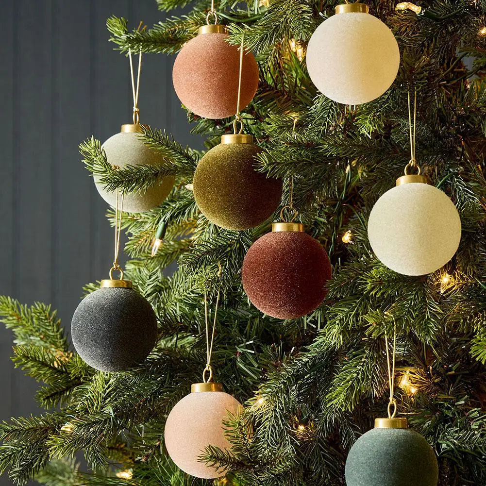 Velvet Christmas baubles in soft muted colors hanging on a lit green tree