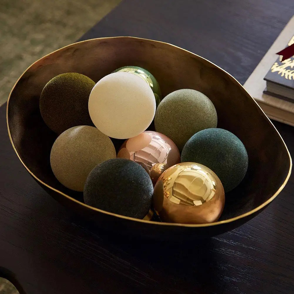 Velvet Christmas baubles piled in a dark bowl on a wooden table