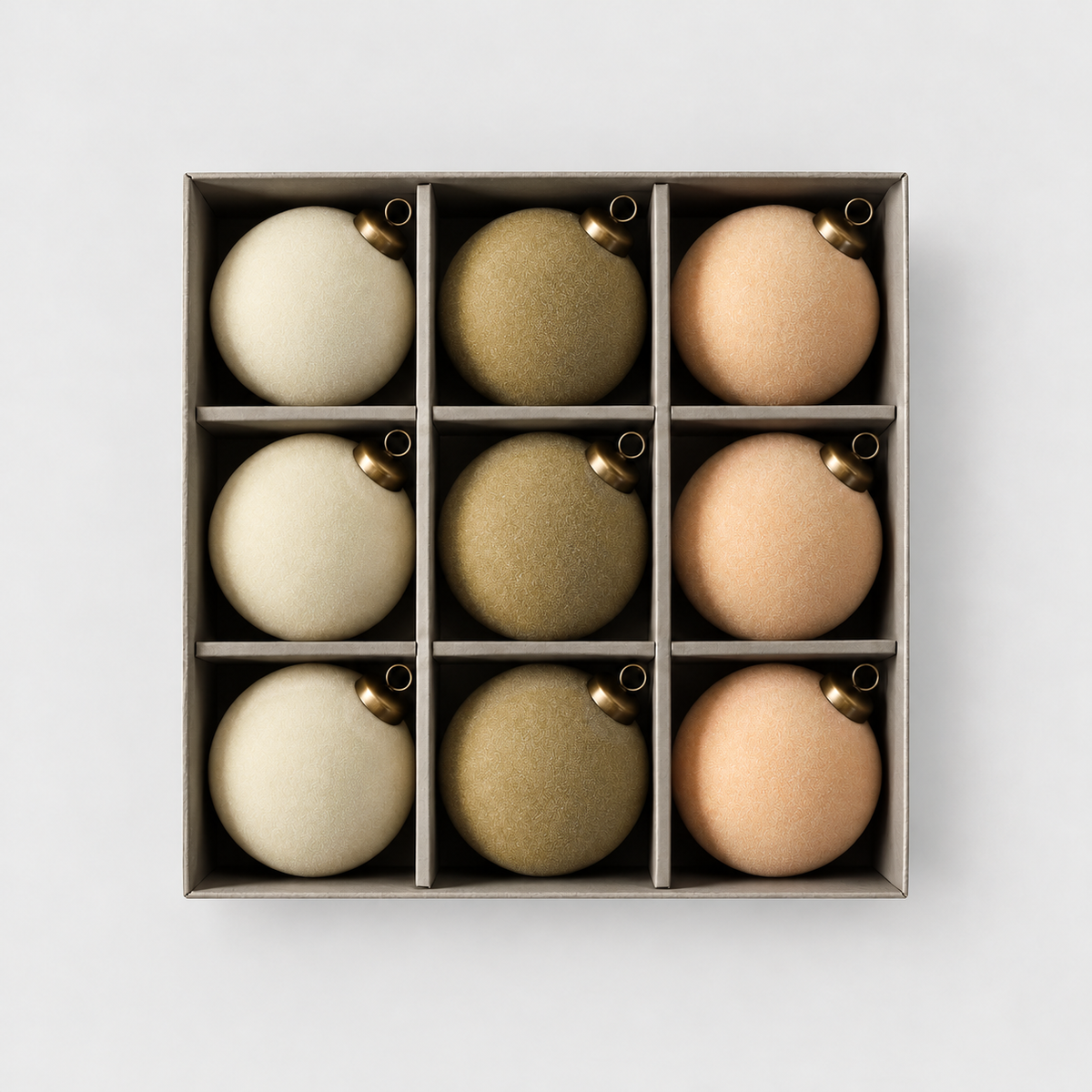 Open box of nine velvet Christmas baubles, three cream, three khaki and three peach, on a light gray background