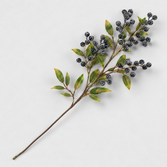Artificial berry branch with slate blue berries and green leaves lying on a light gray background