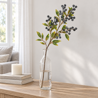 Single blue berry branch standing in a tall glass bottle vase on a console in a bright living room