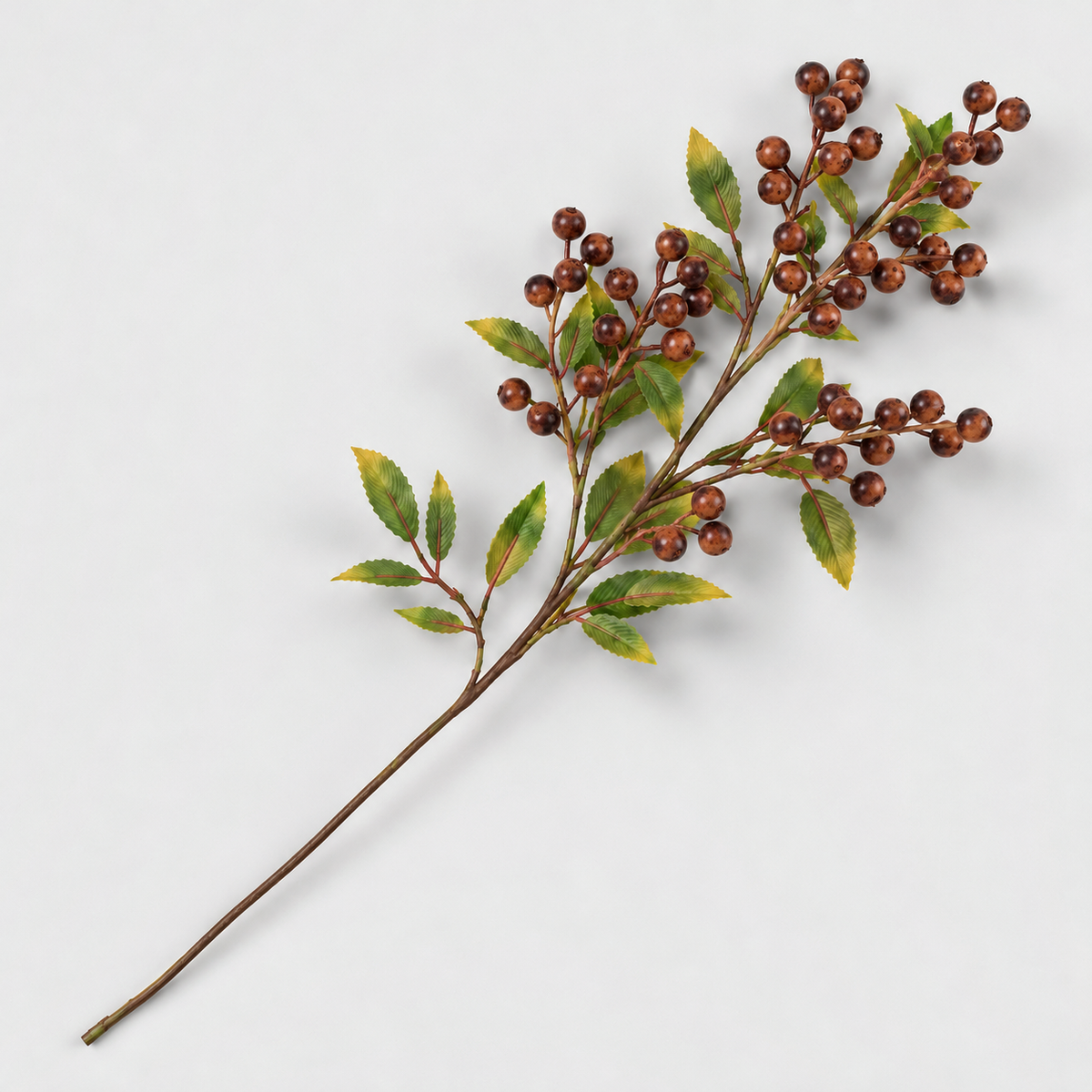 Artificial berry branch with rust brown berries and green leaves lying on a light gray background