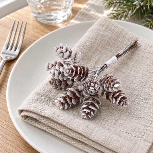 Bundle of frosted pine cone picks lying on a folded linen napkin at a winter table setting