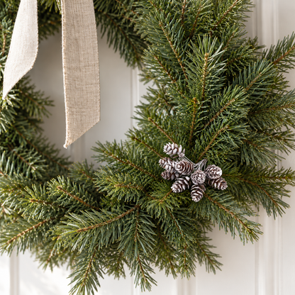 Frosted pine cone picks tucked into a green fir wreath on a white wall
