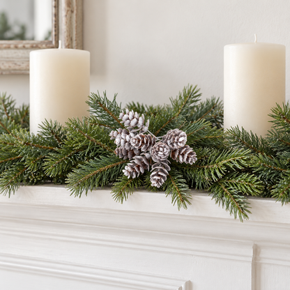 Frosted pine cone picks in a fir garland on a white fireplace mantel beside cream candles