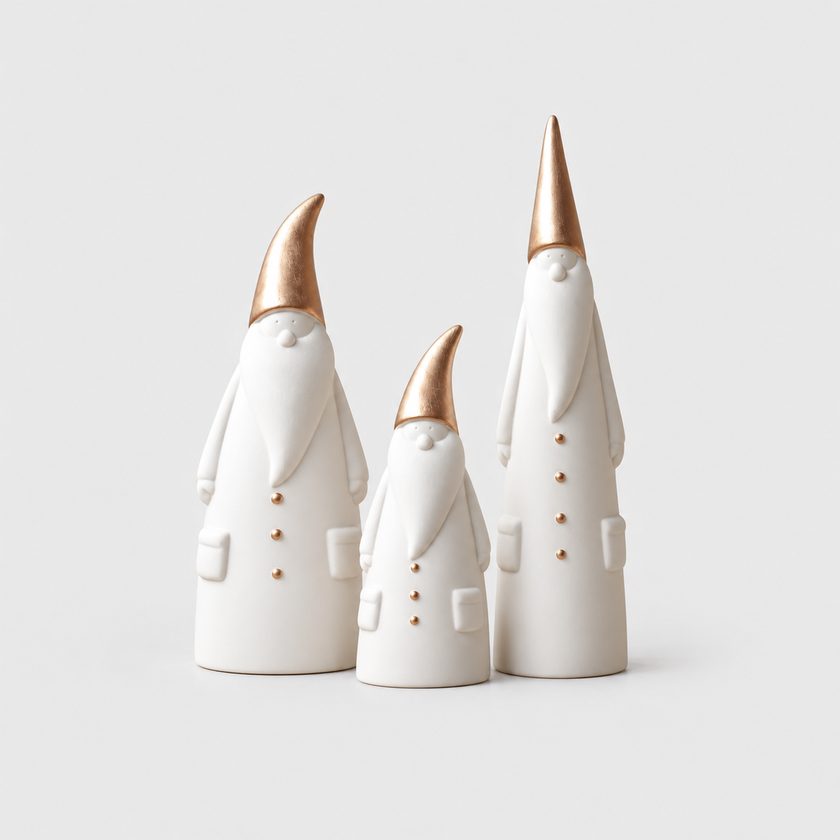 Set of three matte white ceramic Santa figurines in three heights with rose gold hats on a light gray background