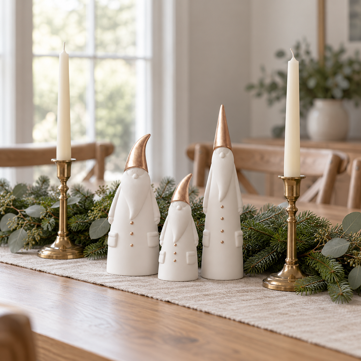 Three ceramic Santa figurines as a centerpiece on a dining table runner with greenery and brass candlesticks