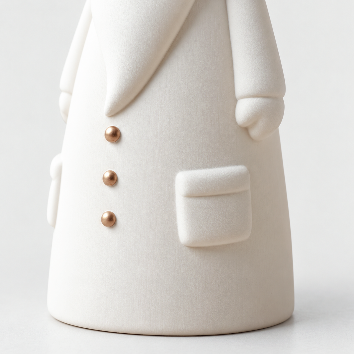 Close-up of the side of a matte white ceramic Santa figurine showing its patch pocket, mitten and gold buttons in relief