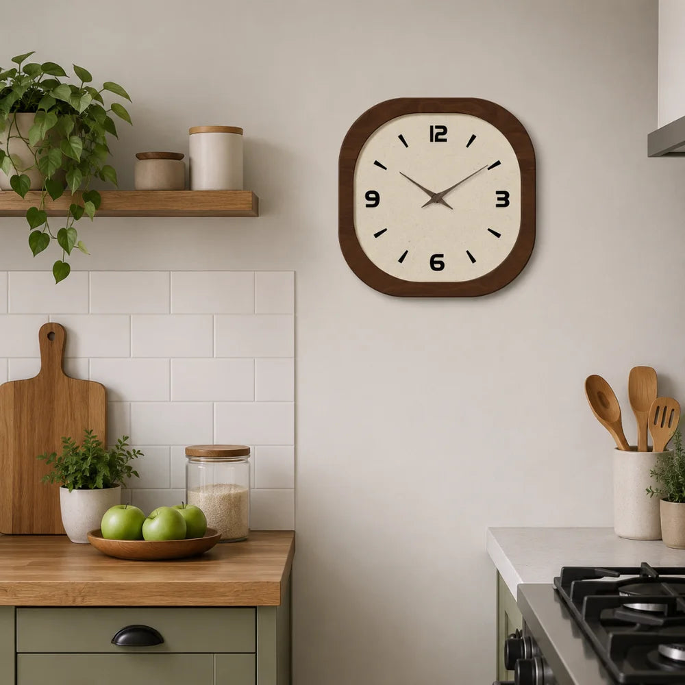 Cream-faced wall clock with a dark wood-look frame on a kitchen wall above a counter with green apples