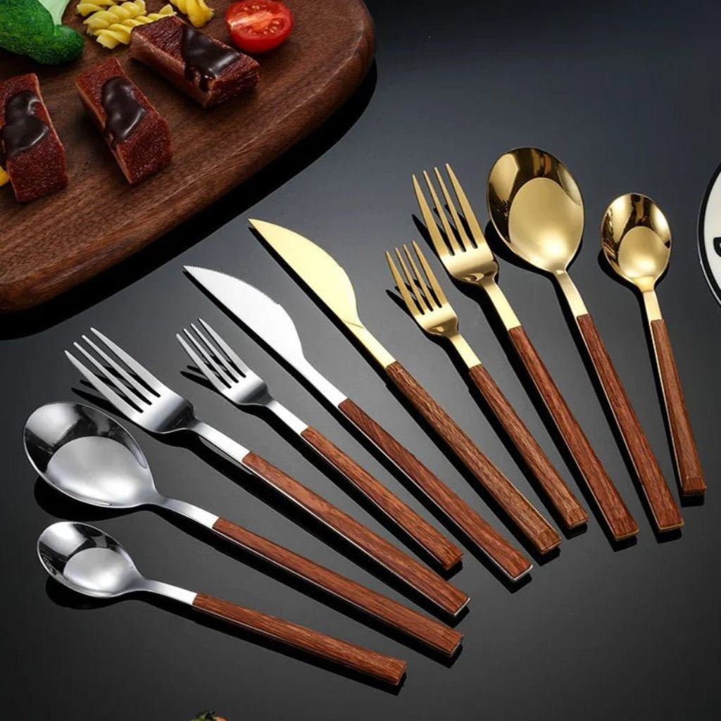 Silver and gold stainless steel cutlery with brown wood-grain handles fanned out on a dark table