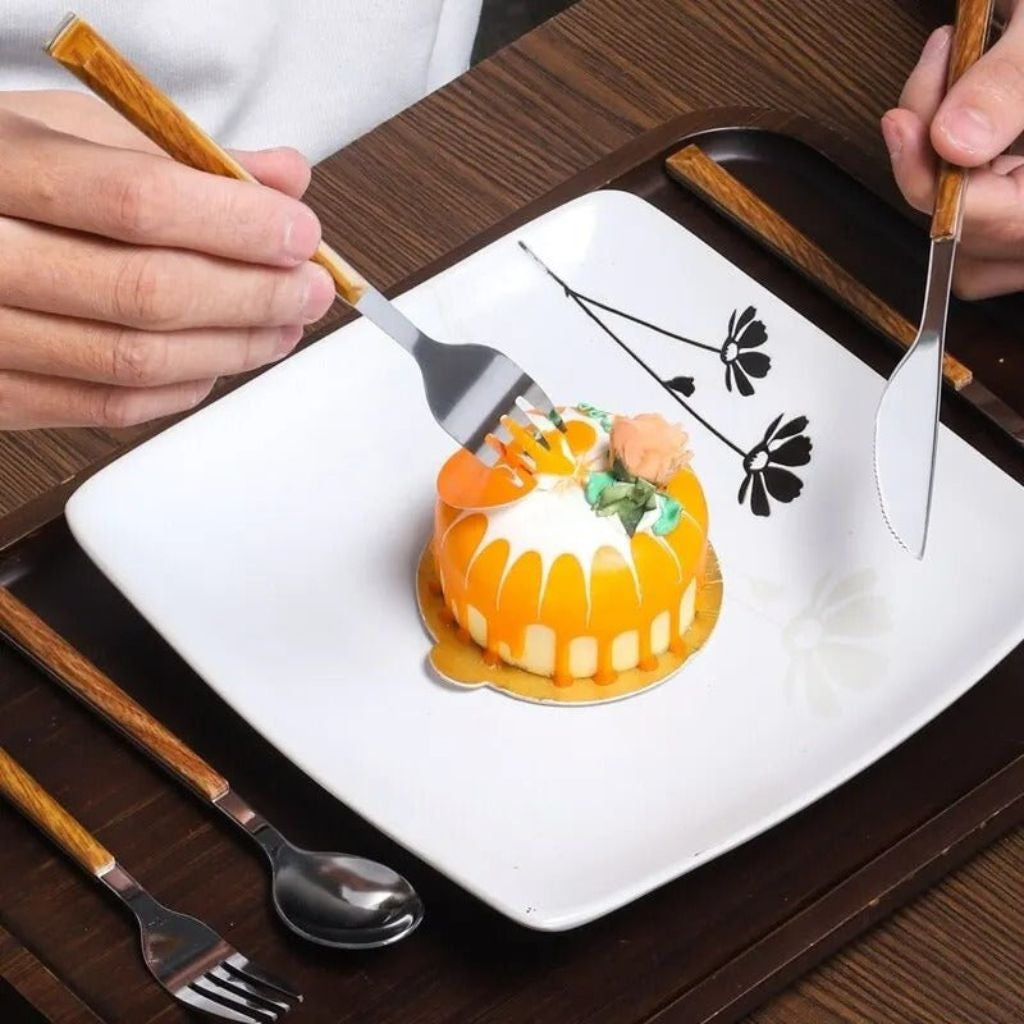 Silver fork and knife with wood-grain handles cutting a small orange cake on a white plate