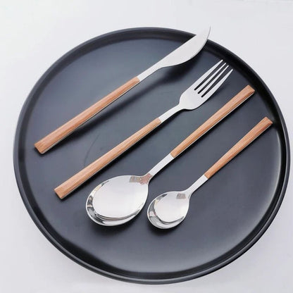 Silver knife, fork, soup spoon and teaspoon with wood-look handles on a round black plate