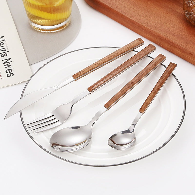 Silver cutlery with wood-grain handles laid across a clear glass plate on a white table