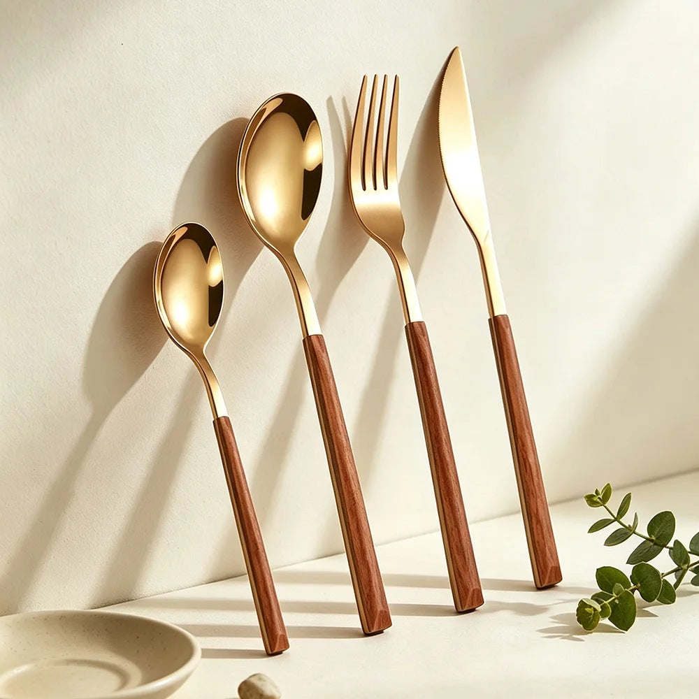 Gold teaspoon, soup spoon, fork and knife with wood-look handles leaning against a cream wall