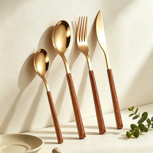 Gold teaspoon, soup spoon, fork and knife with wood-look handles leaning against a cream wall