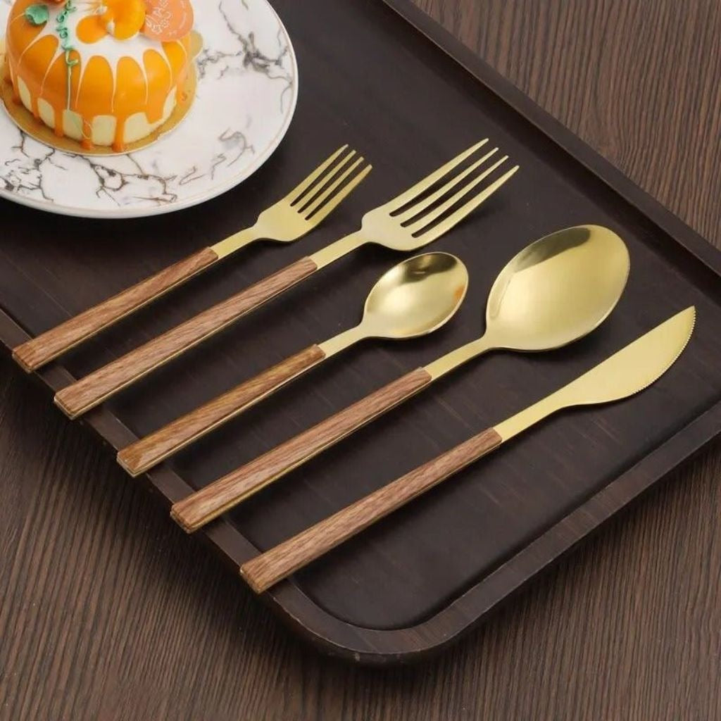 Gold cutlery set with wood-look handles: knife, soup spoon, teaspoon, fork and dessert fork on a dark tray