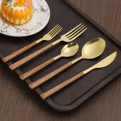 Gold cutlery set with wood-look handles: knife, soup spoon, teaspoon, fork and dessert fork on a dark tray