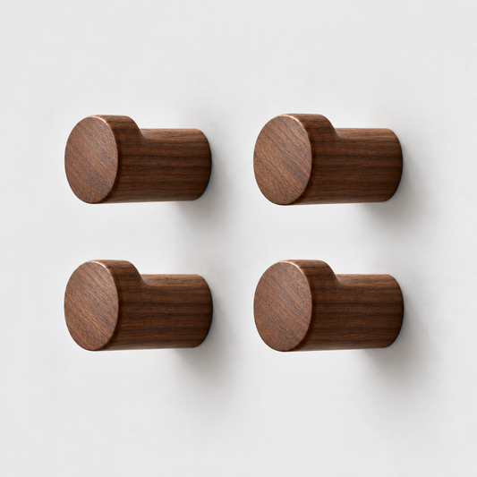 Set of four walnut wood wall hooks in a two by two grid on a plain light gray wall, seen from a three-quarter front view