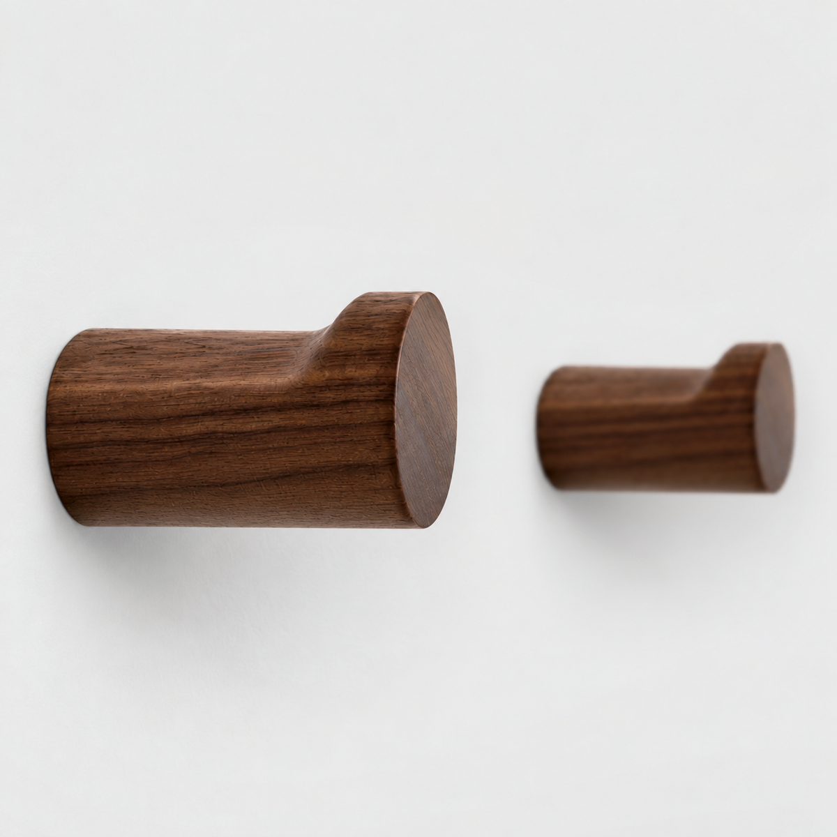 Close-up of walnut wall hooks showing the wood grain, the flat ledge on top and the raised lip at the end