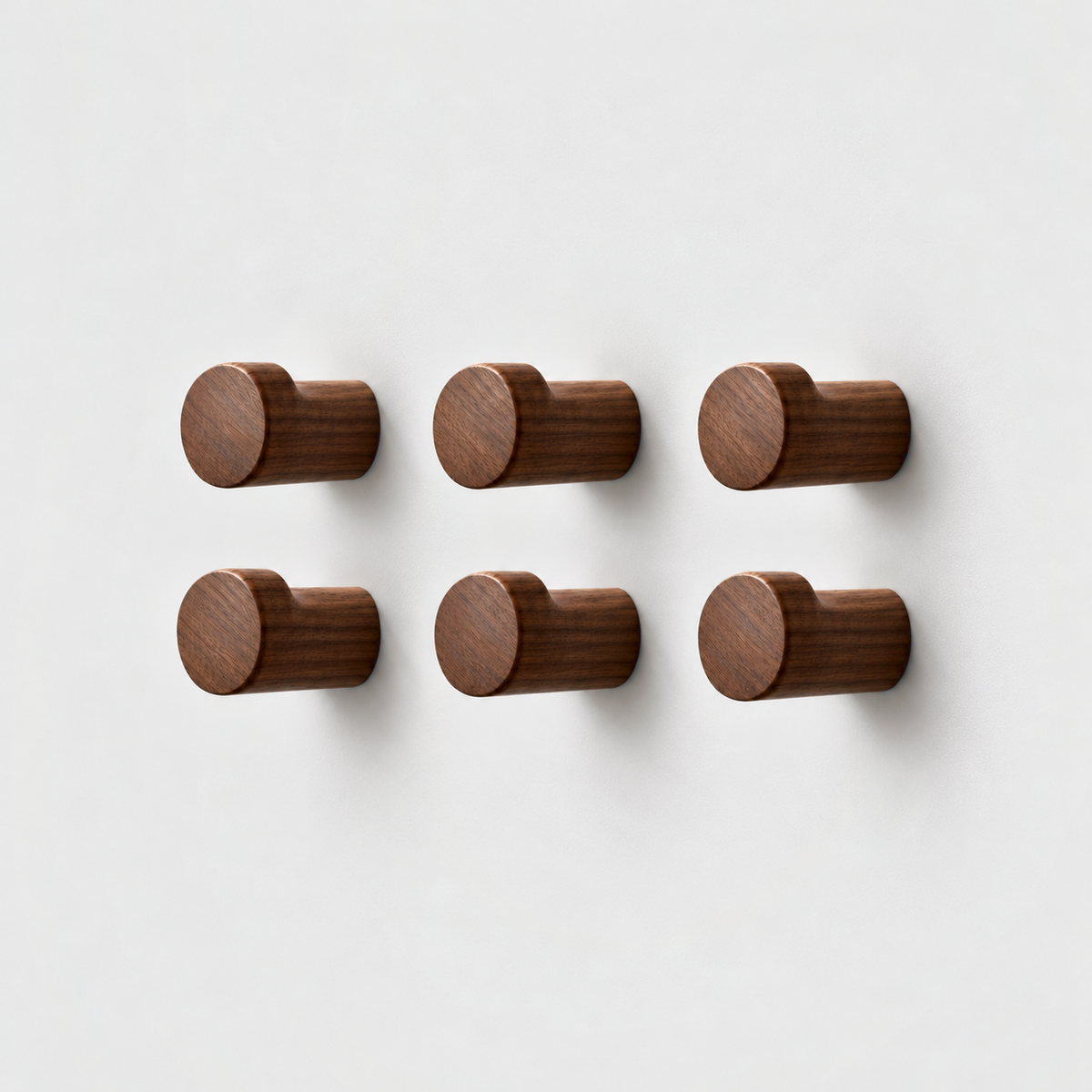 Set of six walnut wood wall hooks in three columns and two rows on a plain light gray wall, seen from a three-quarter front view