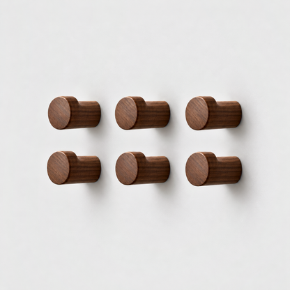 Set of six walnut wood wall hooks in three columns and two rows on a plain light gray wall, seen from a three-quarter front view