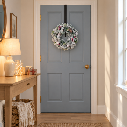 Large frosted pine wreath with berries and pine cones hanging on a blue-grey door in a hallway