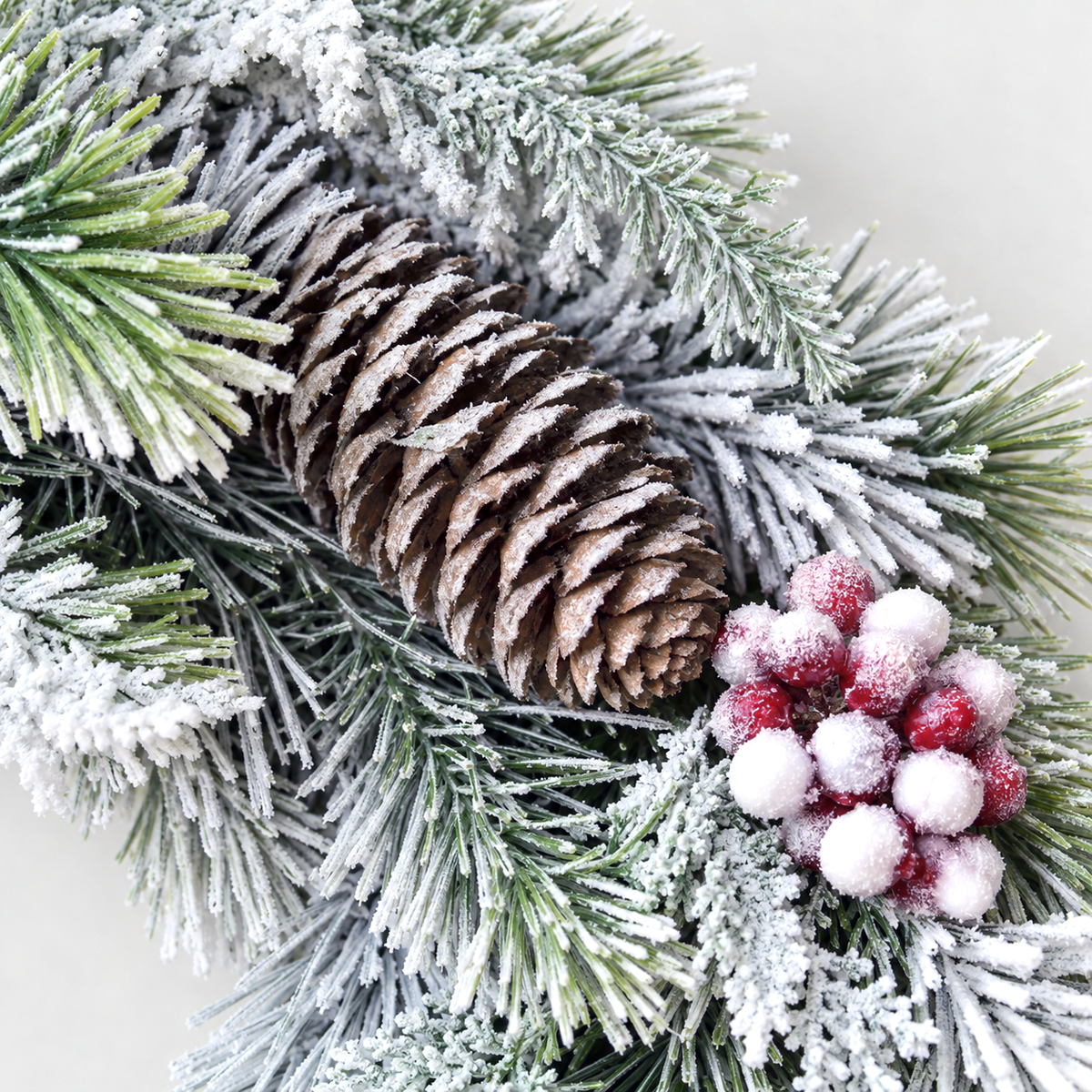 Close-up of a frosted pine cone and a cluster of frosted red and white berries on the wreath