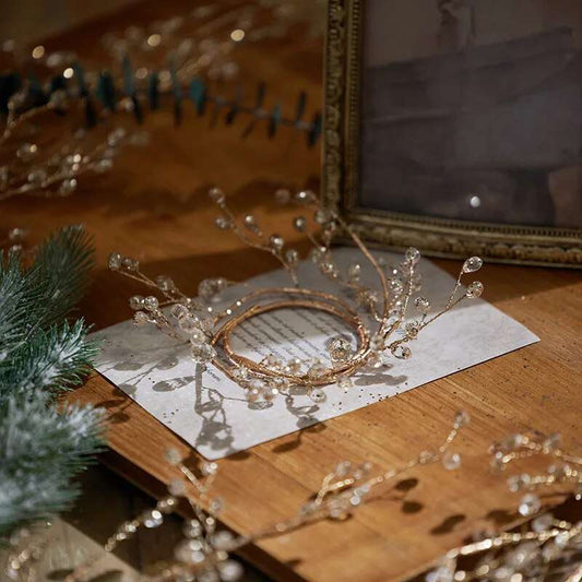 Gold crystal bead napkin ring lying flat on a printed card on a wooden table, beside a picture frame and pine greenery