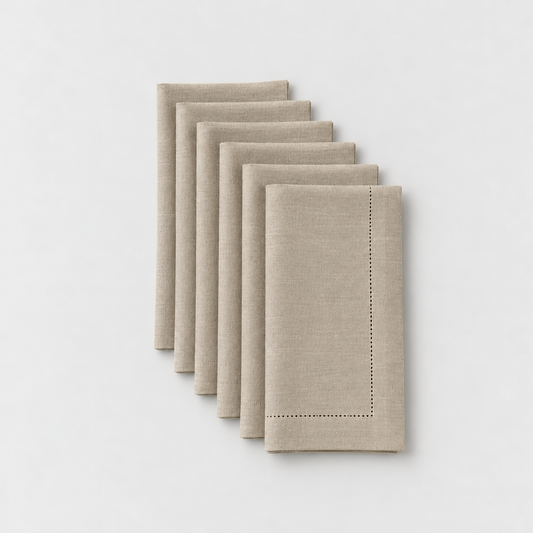 Six folded taupe hemstitch dinner napkins laid in a staggered row on a light grey background