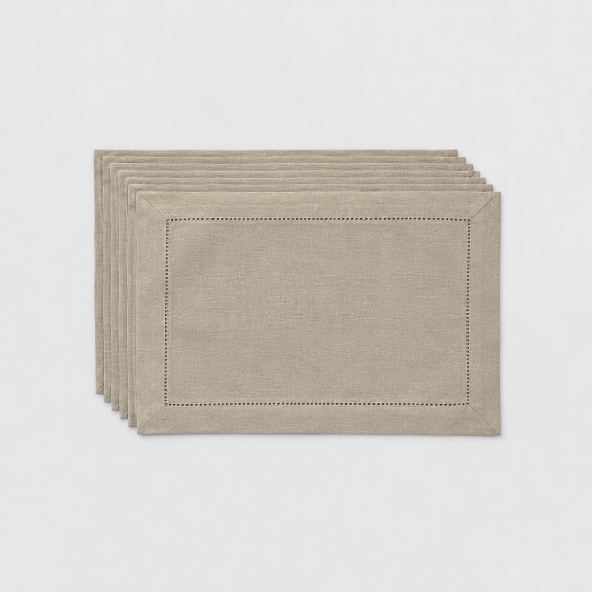 A thin stack of six taupe hemstitch placemats on a light grey background