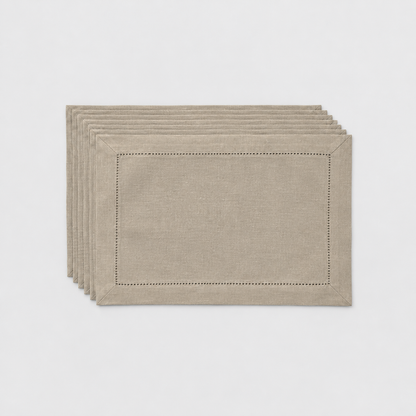 A thin stack of six taupe hemstitch placemats on a light grey background