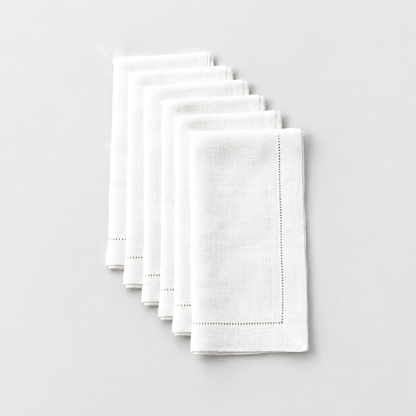 Six folded white hemstitch dinner napkins laid in a staggered row on a light grey background