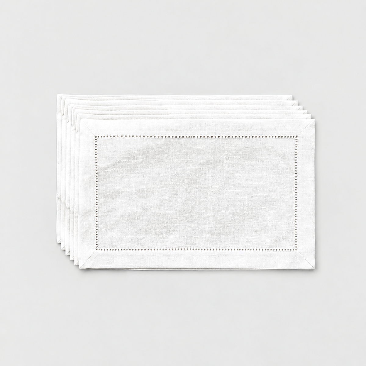 A thin stack of six white hemstitch placemats on a light grey background