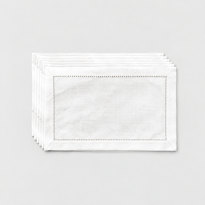 A thin stack of six white hemstitch placemats on a light grey background