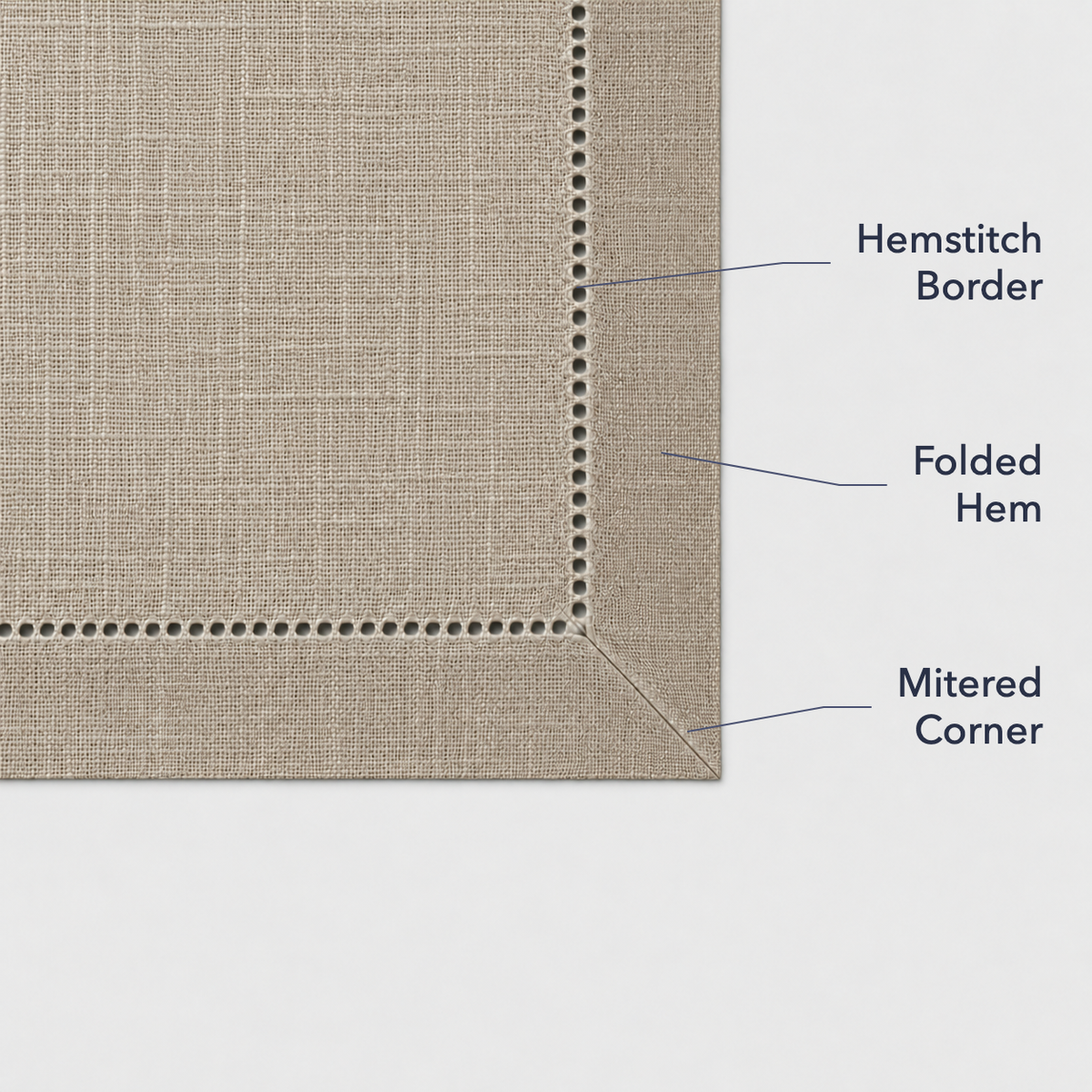 Close-up of a taupe placemat corner showing the open hemstitch border, the folded hem and the mitered corner