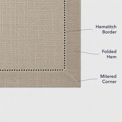 Close-up of a taupe placemat corner showing the open hemstitch border, the folded hem and the mitered corner