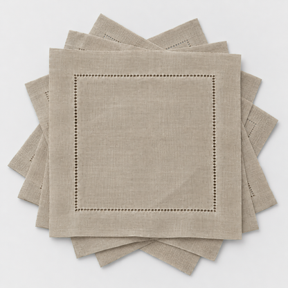 Six small taupe hemstitch cocktail napkins fanned out in a loose rotation on a light grey background