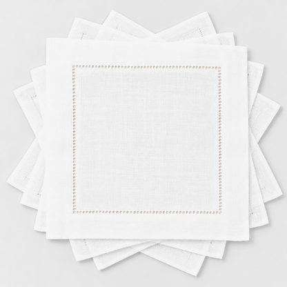 Six small white hemstitch cocktail napkins fanned out in a loose rotation on a light grey background