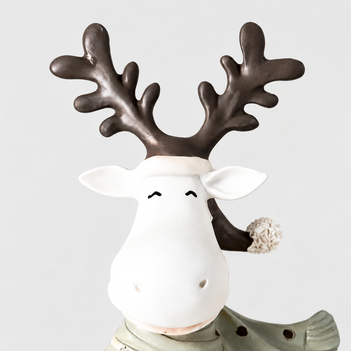 Close-up of the reindeer figurine's closed smiling eyes, white hat band with pompom, pointed ears and brown antlers