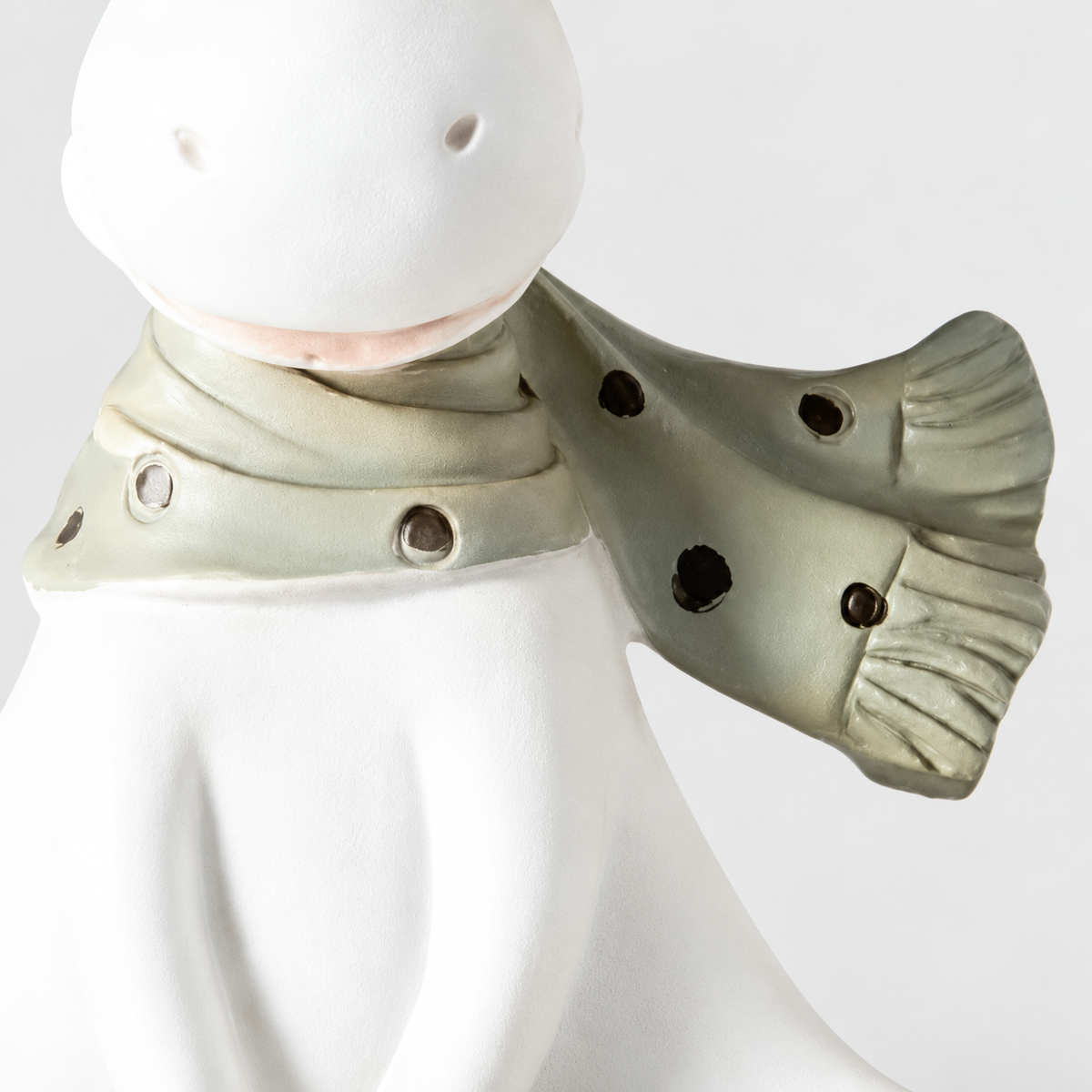 Close-up of the reindeer figurine's green-gray scarf with dark dots and a fringed end