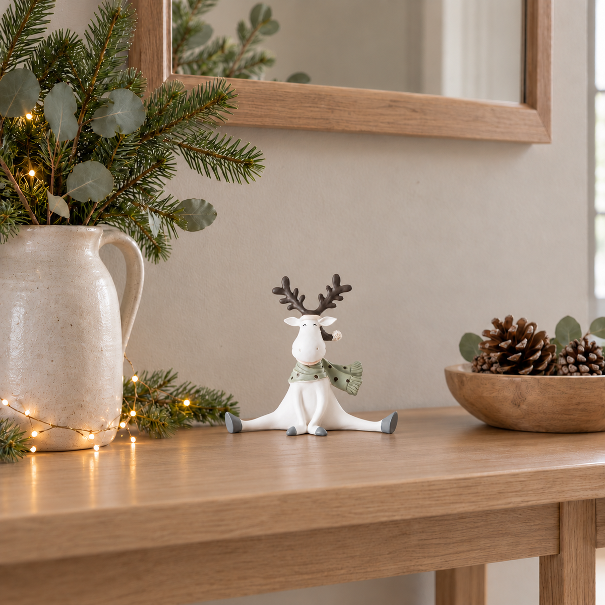 White reindeer figurine on an oak hall console beside a stoneware jug of fir stems and a bowl of pine cones