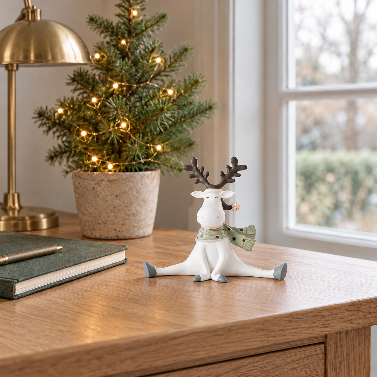 Reindeer figurine on the corner of an oak desk beside a notebook and a small potted fir tree with warm lights