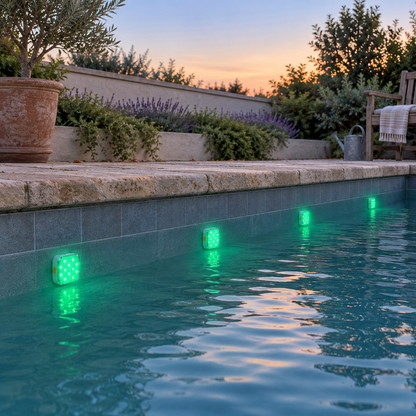 Four square pool lights glowing emerald green along the wall of a small courtyard plunge pool at dusk
