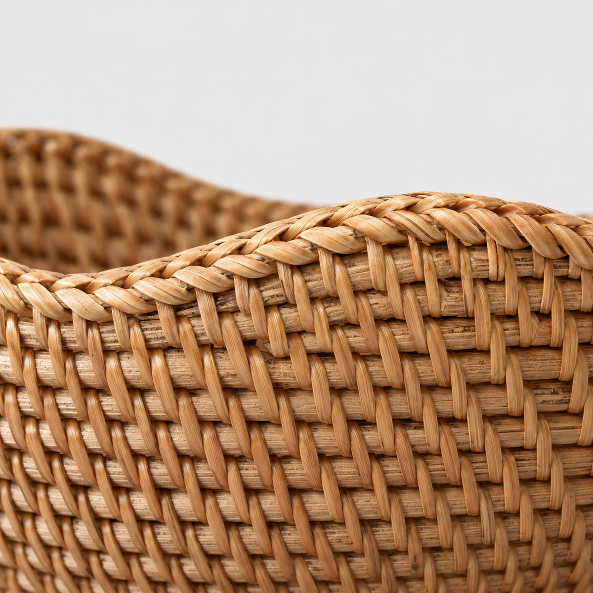 Close-up of the rattan bowl's wavy rim bound in fine strands and the rows of small slanted stitches in its wall