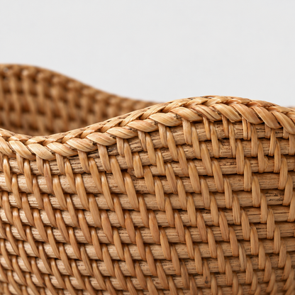 Close-up of the rattan bowl's wavy rim bound in fine strands and the rows of small slanted stitches in its wall