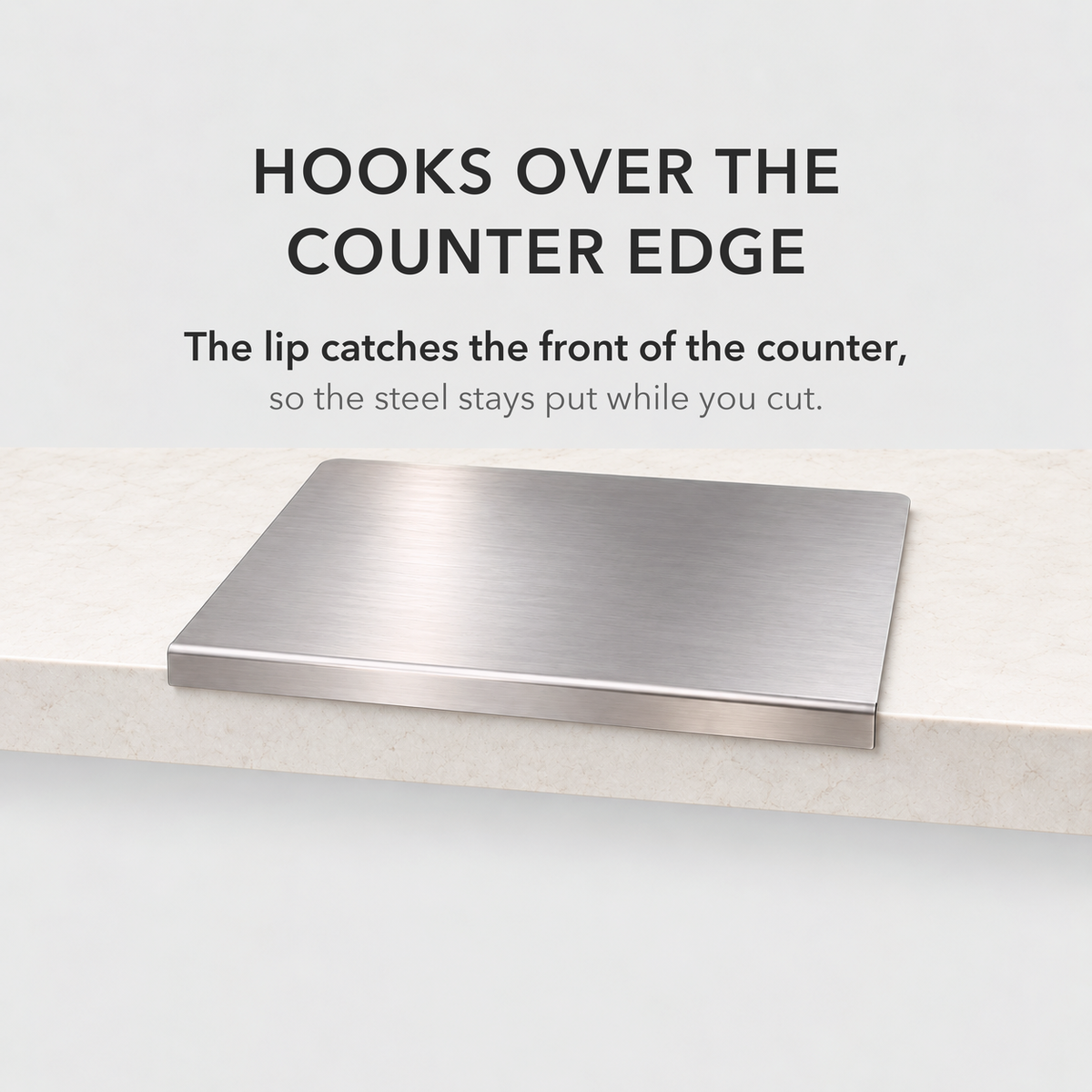 Steel chopping board with its folded lip hooked over the front edge of a stone counter
