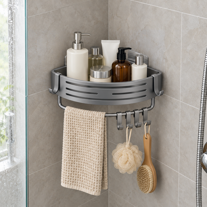Gray aluminum corner basket holding shampoo bottles in a tiled shower corner, a beige towel over the bar below it and a loofah and a brush on its sliding hooks