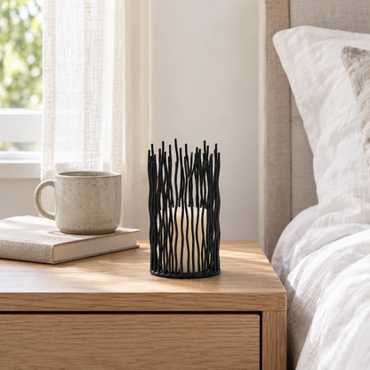 One small black iron candle holder with an ivory pillar candle on an oak bedside table by a window